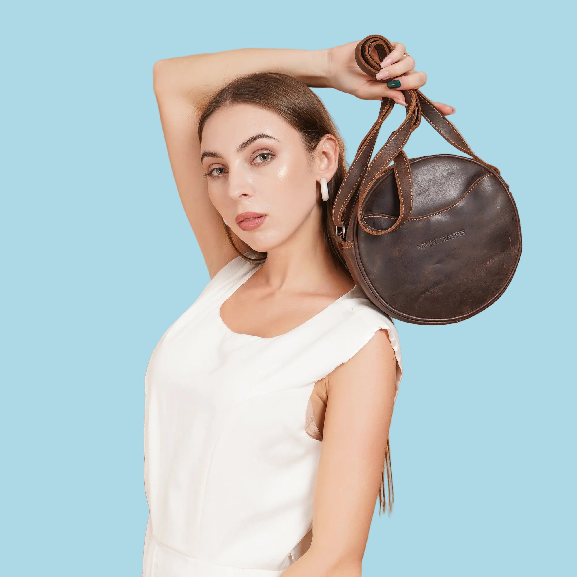 Minori Leather Luna leather round crossbody bag in chestnut, brown, and hair-on brown with adjustable strap and sleek design.